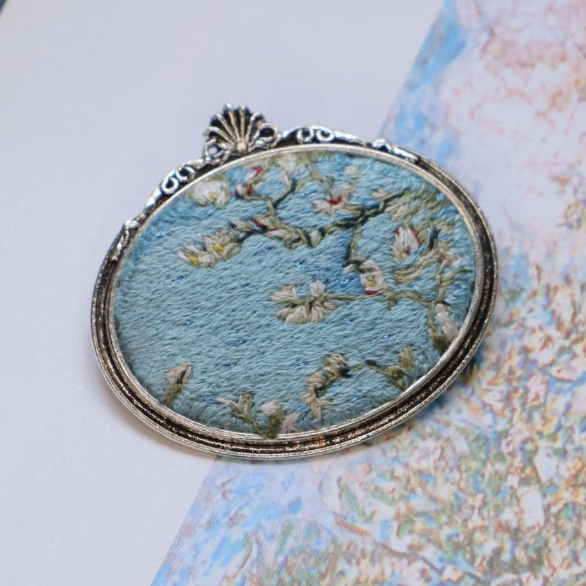 Hand embroidered brooch  featuring white blossoms against a blue sky, handcrafted textile jewelry and wearable art by Mina.