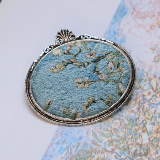 Hand embroidered brooch  featuring white blossoms against a blue sky, handcrafted textile jewelry and wearable art by Mina.