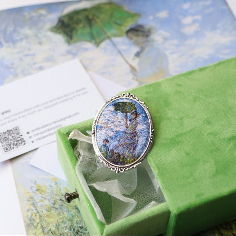 Hand embroidered brooch inspired by Claude Monet, featuring a woman with a green parasol in an Impressionist landscape, handcrafted textile jewelry and wearable art by Mina.