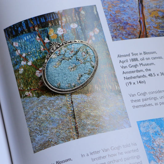 Hand embroidered brooch inspired by Vincent van Gogh's flowering branches, featuring white blossoms against a blue sky, handcrafted textile jewelry and wearable art by Mina.
