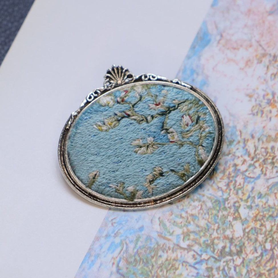 Hand embroidered brooch inspired by Vincent van Gogh's flowering branches, featuring white blossoms against a blue sky, handcrafted textile jewelry and wearable art by Mina.