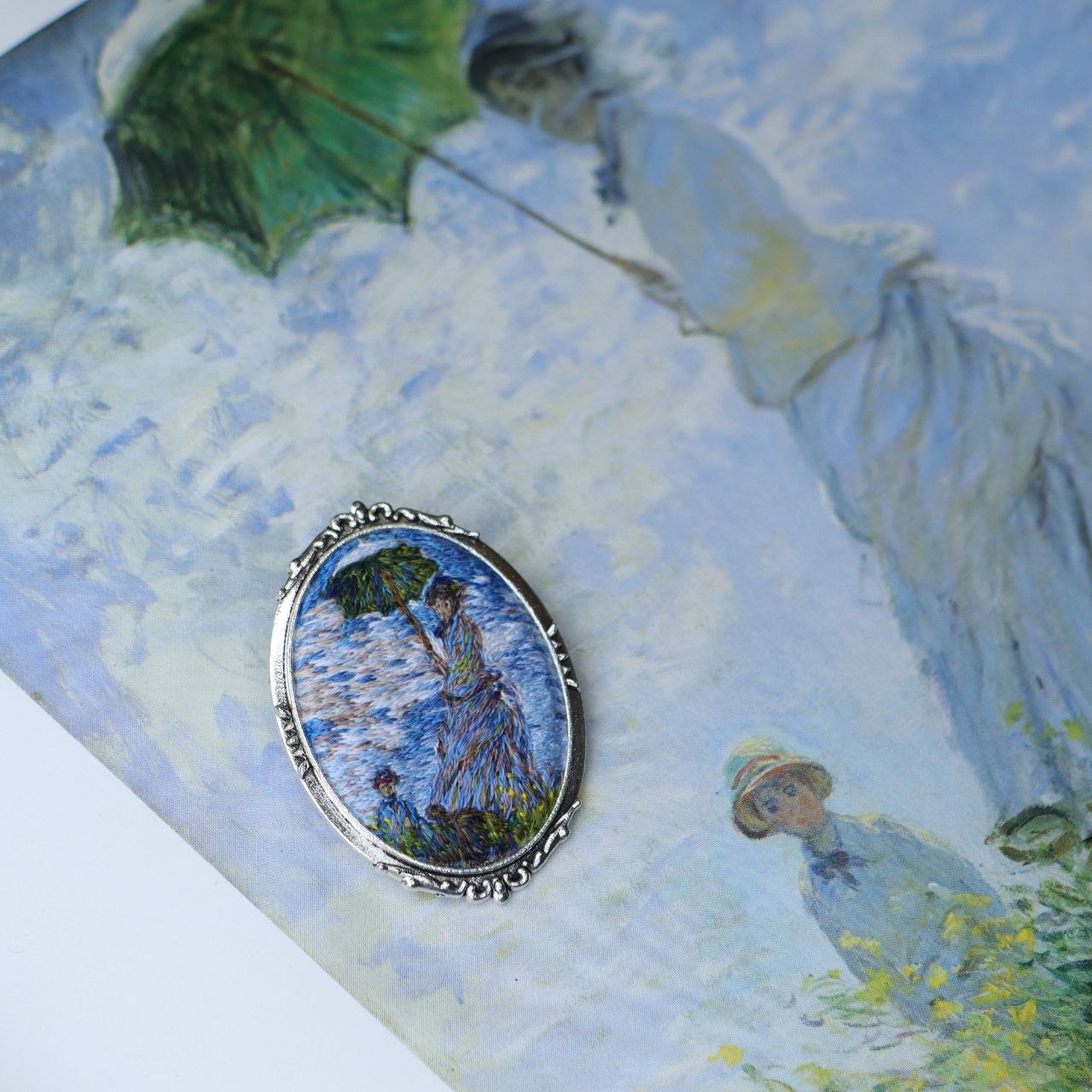 Hand embroidered brooch inspired by Claude Monet, featuring a woman with a green parasol in an Impressionist landscape, handcrafted textile jewelry and wearable art by Mina.