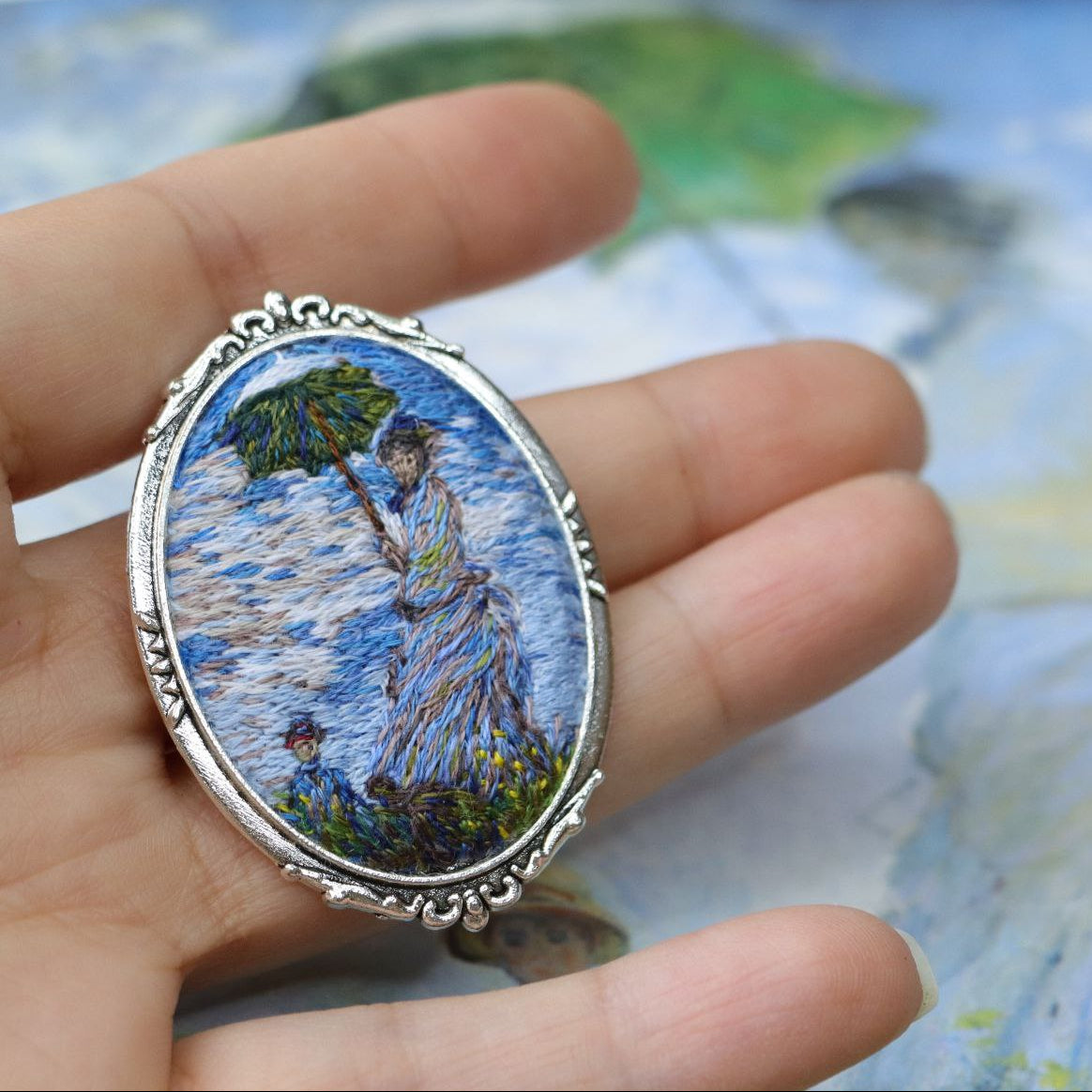 Hand embroidered brooch inspired by Claude Monet, featuring a woman with a green parasol in an Impressionist landscape, handcrafted textile jewelry and wearable art by Mina.